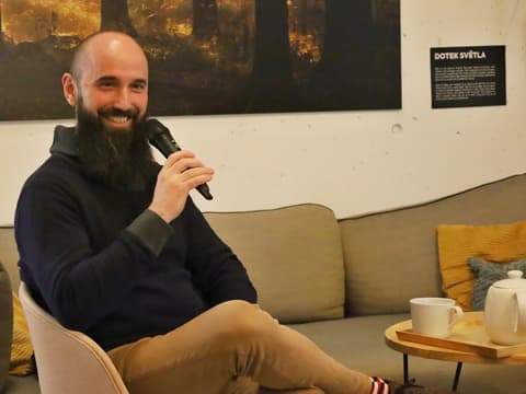 Beseda s Pavlem Polou: host s mikrofonem se usmívá na pohovce